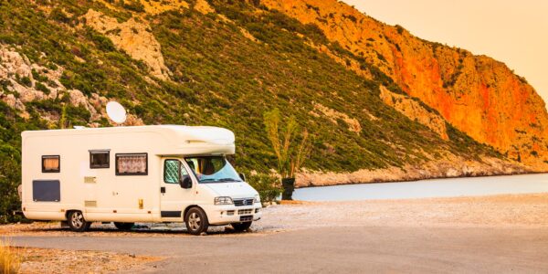 An RV with a satellite parked next to a lake.